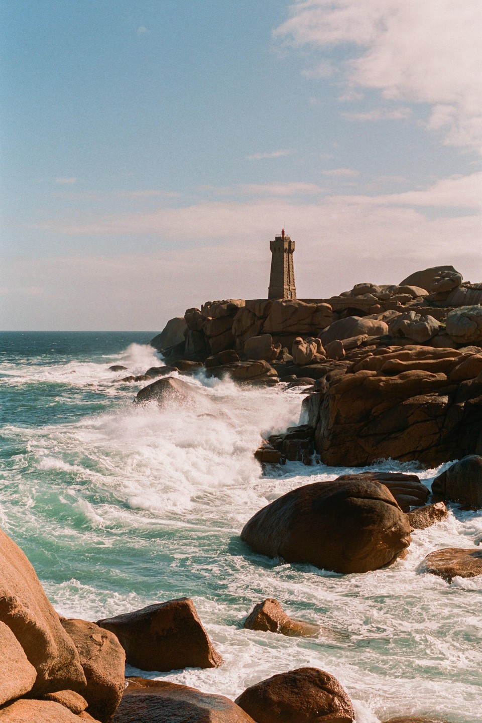 A lighthouse stands on a rocky coast with waves crashing against the shore.
