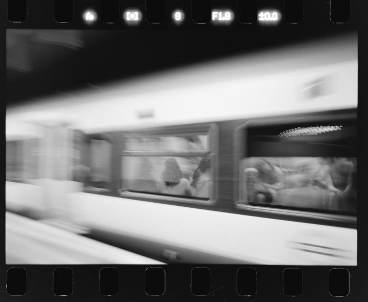 A blurry black and white image shows the side of a moving train with people visible through the windows.