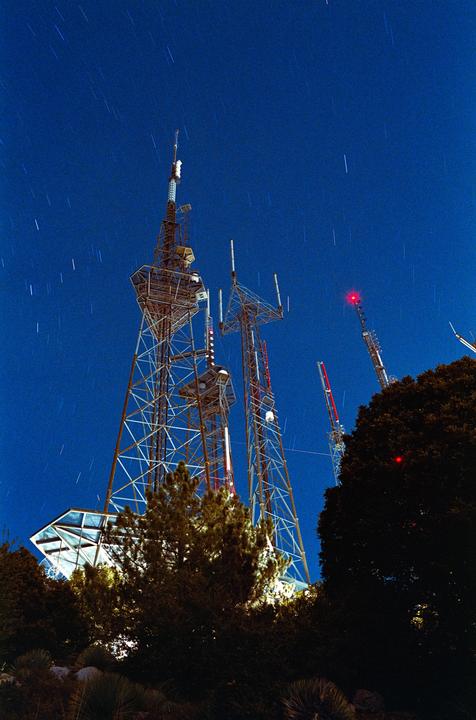 Several tall radio towers with red lights are visible against a deep blue night sky with star trails.
