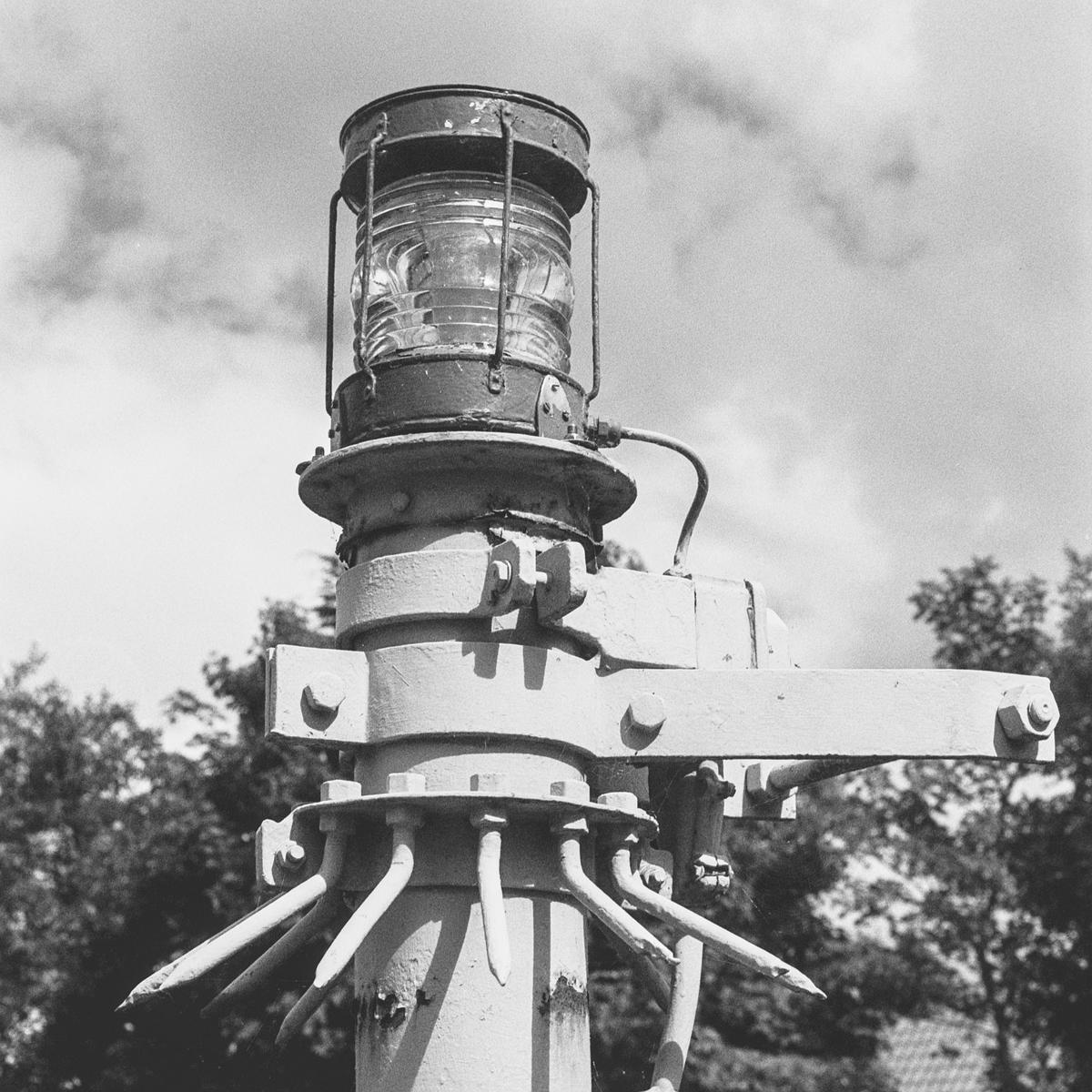 A black and white close-up shows a light fixture on a pole against a cloudy sky.