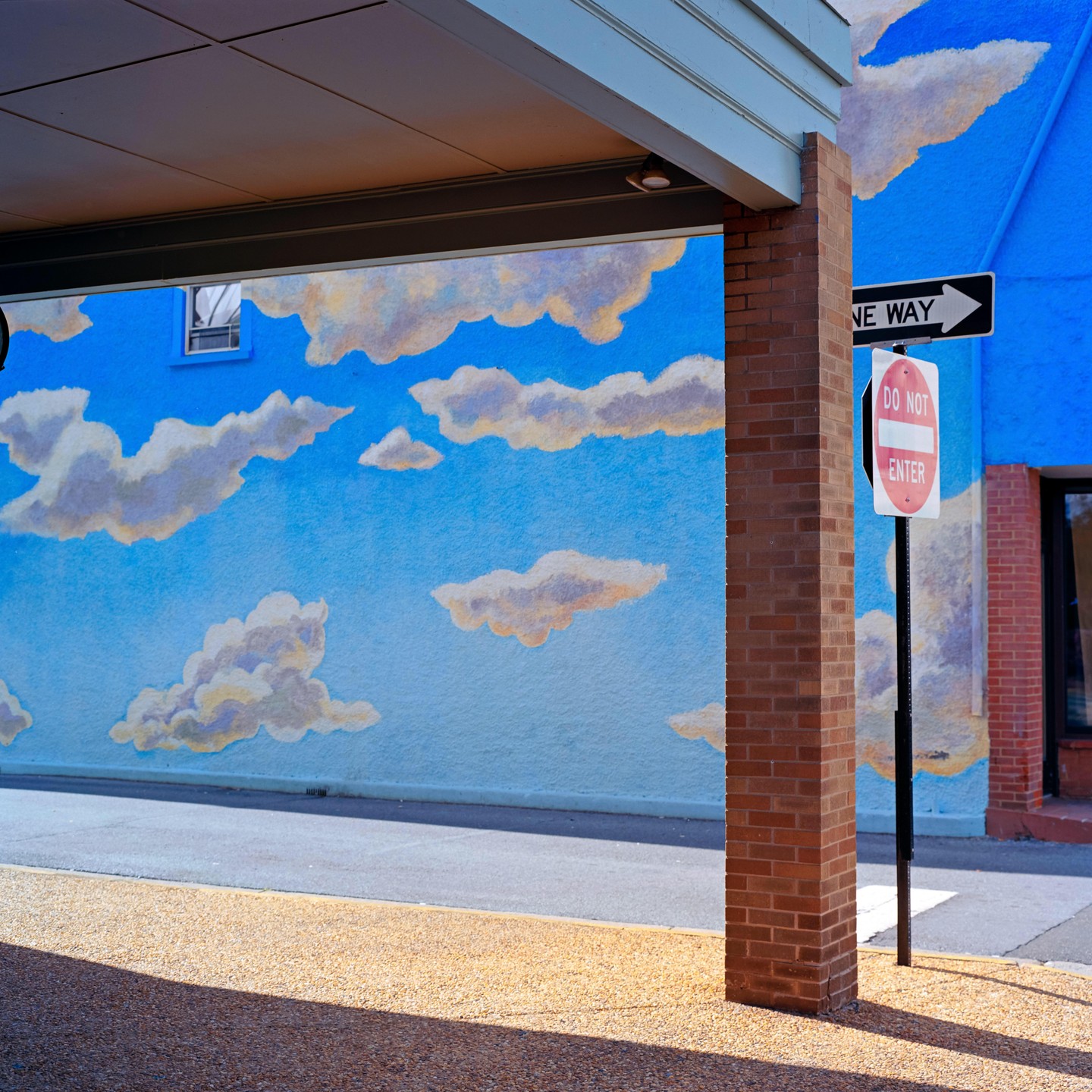 A blue wall with painted clouds is next to a brick column and a "Do Not Enter" sign.