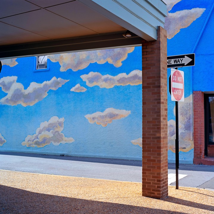 A blue wall with painted clouds is next to a brick column and a "Do Not Enter" sign.