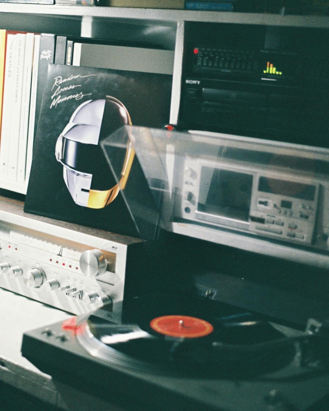A record player with a red record is next to a Daft Punk album cover and other stereo equipment.