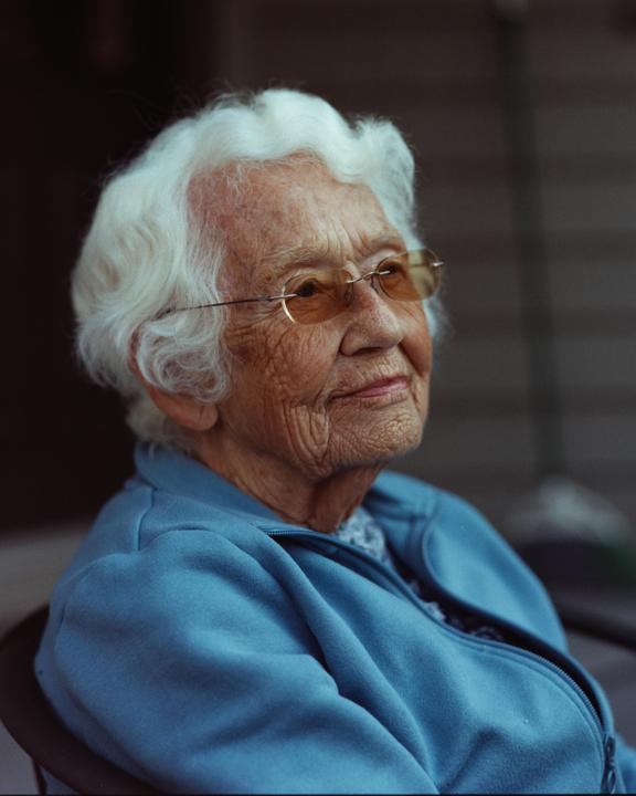 A woman with white hair and glasses is looking up and to the right.