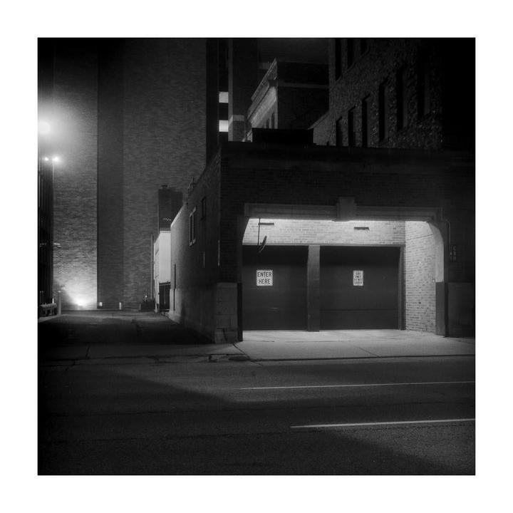 A street at night leads to a building with two garage doors, one with an "enter here" sign.