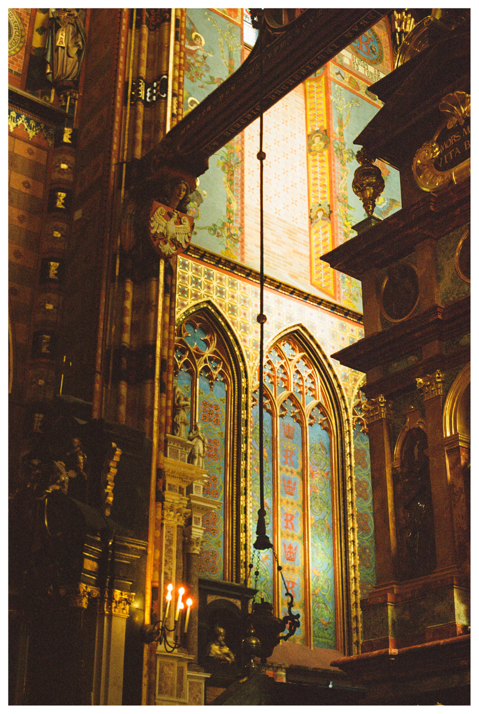 A richly decorated basilica interior features ornate arched windows and a candelabra with lit candles.