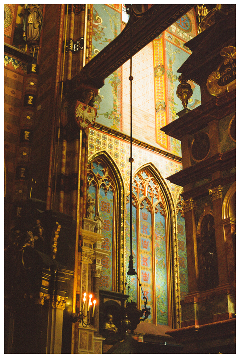 A richly decorated basilica interior features ornate arched windows and a candelabra with lit candles.