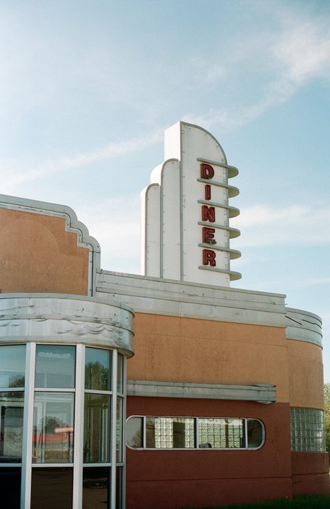 A diner with a tall sign spelling "DINER" vertically is shown under a clear sky.