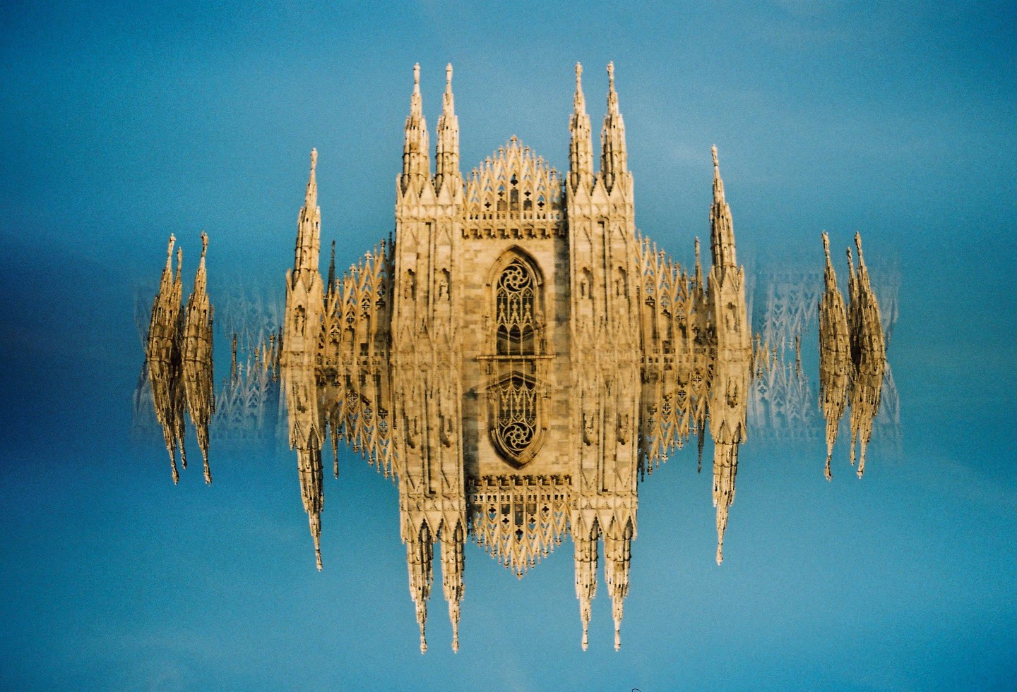 The Duomo di Milano is shown in a double exposure against a blue sky.