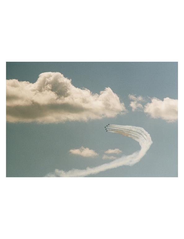 A group of jets flies in formation, leaving white contrails in the blue sky with scattered clouds.