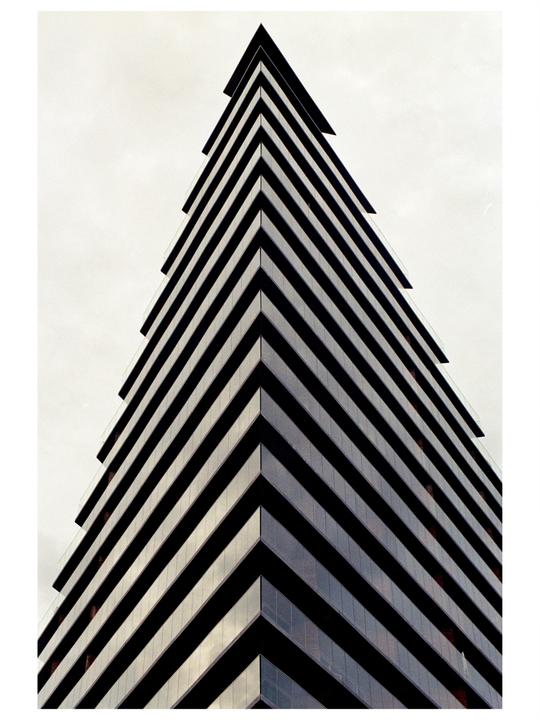 A tall, modern building with a sharp, angular facade points towards the sky.