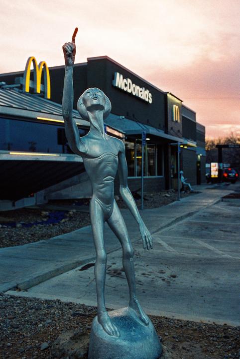A silver alien statue stands in front of a McDonald's restaurant at dusk.