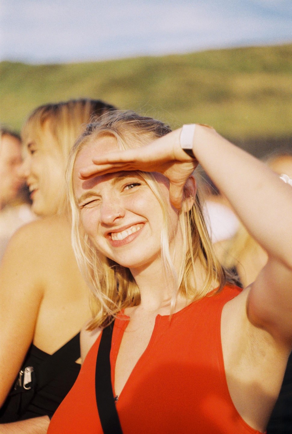 A woman in a red top shields her eyes from the sun and winks at the camera.