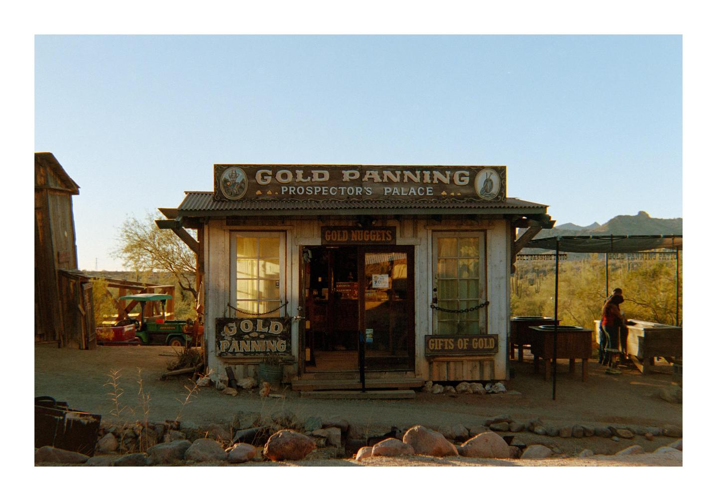 A small wooden building with a "Gold Panning" sign on its facade stands in a desert landscape.