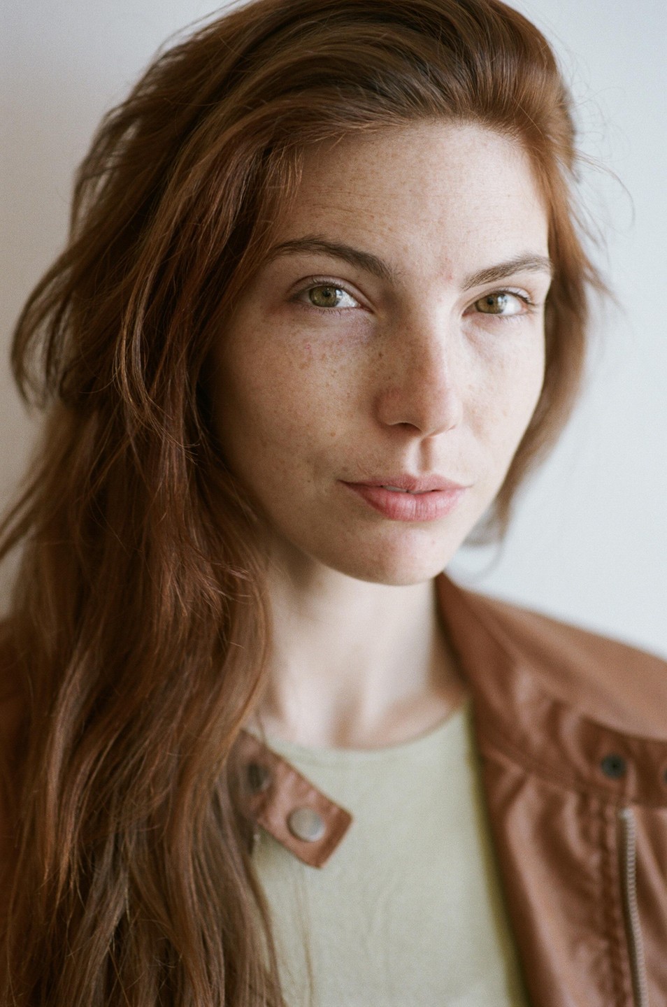 A woman with long red hair and freckles looks directly at the viewer.