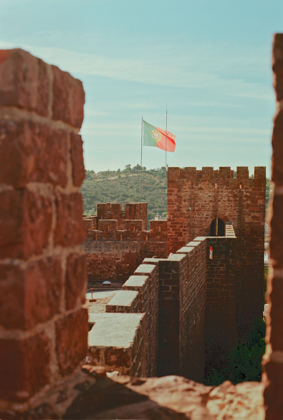 A Portuguese flag flies above the battlements of a historic brick castle.