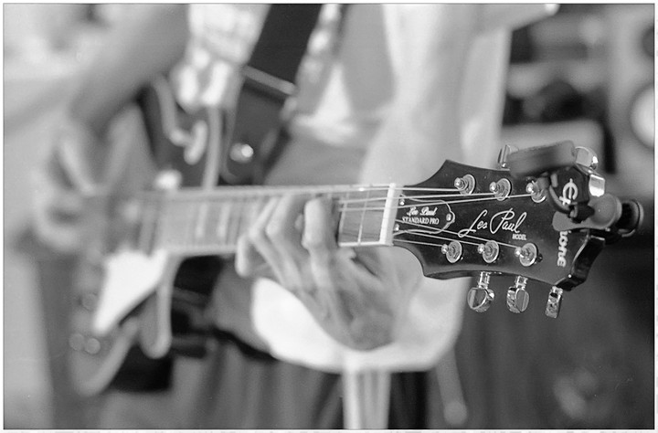 A person's hands are playing an electric guitar, with the headstock in sharp focus.