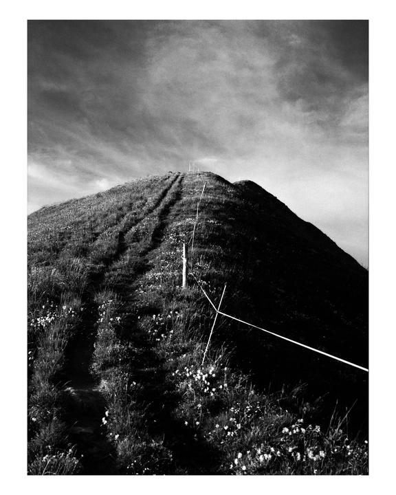 A narrow path leads up a grassy hill towards the sky, with a fence running alongside it.