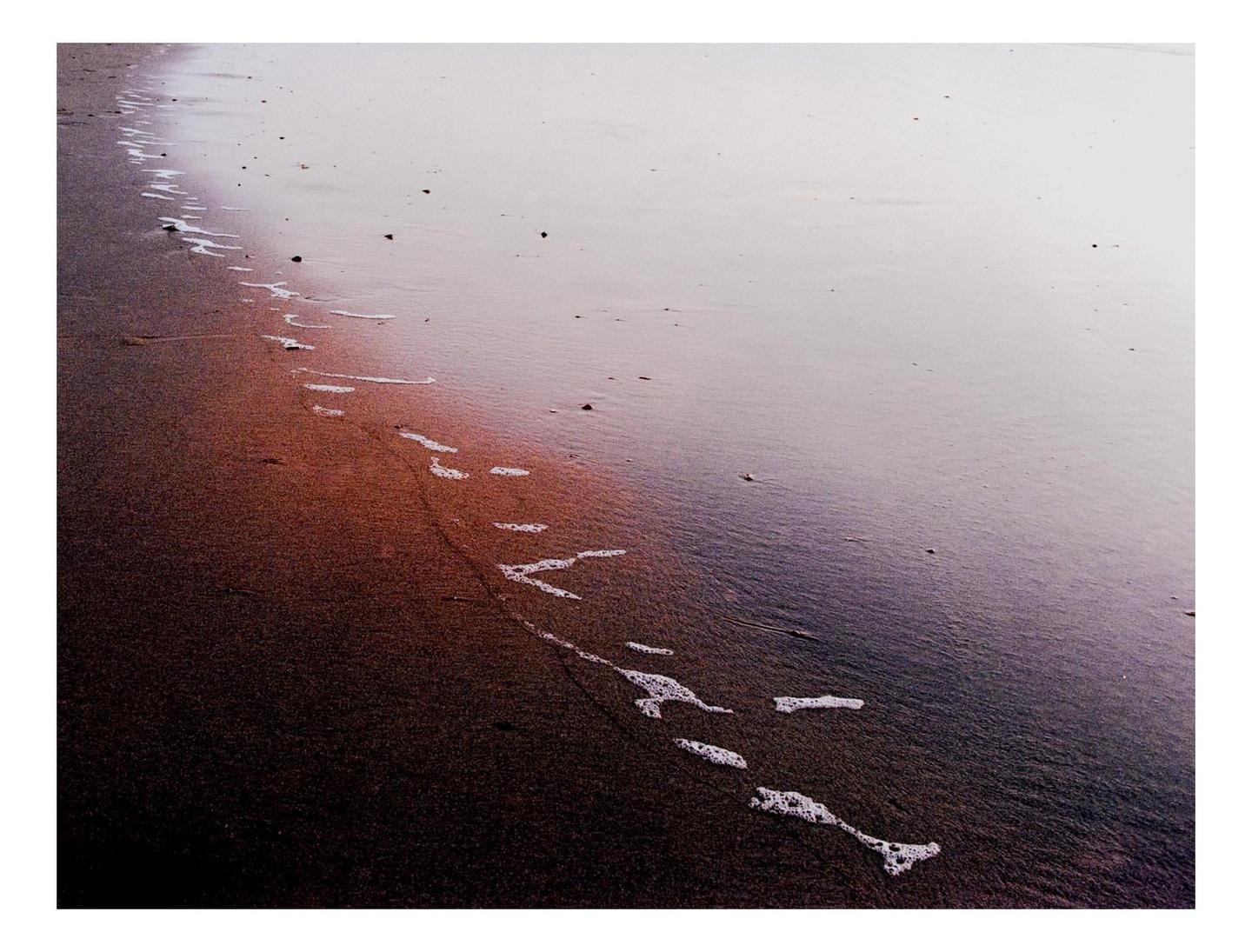 A line of seafoam marks the edge of the water on a sandy beach.