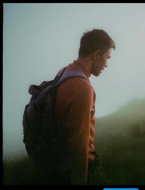 A man with a backpack stands in a hazy, green landscape.