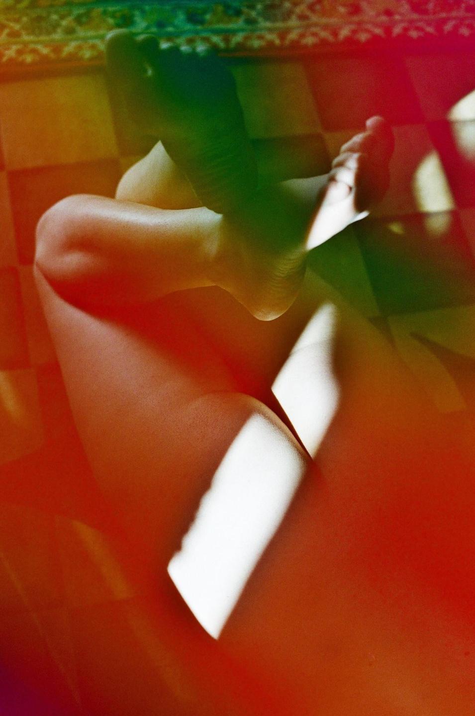 A person's legs and feet are visible on a tiled floor with colorful light leaks and strong shadows.