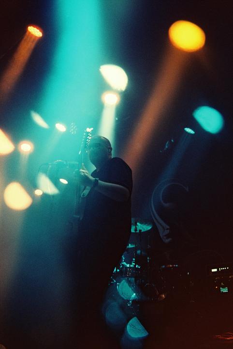 A man plays guitar on a stage illuminated by colorful spotlights.