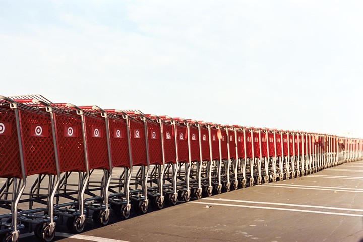 A long line of red shopping carts with white bullseye logos is parked in a parking lot under a bright sky.