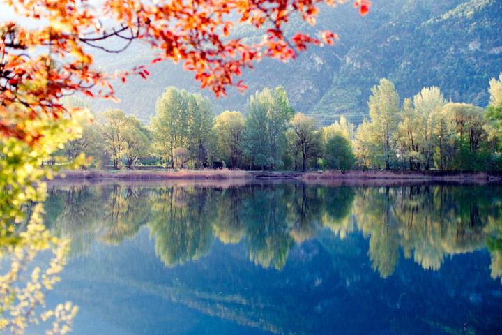 Red and yellow leaves frame a lake reflecting trees and a mountain.