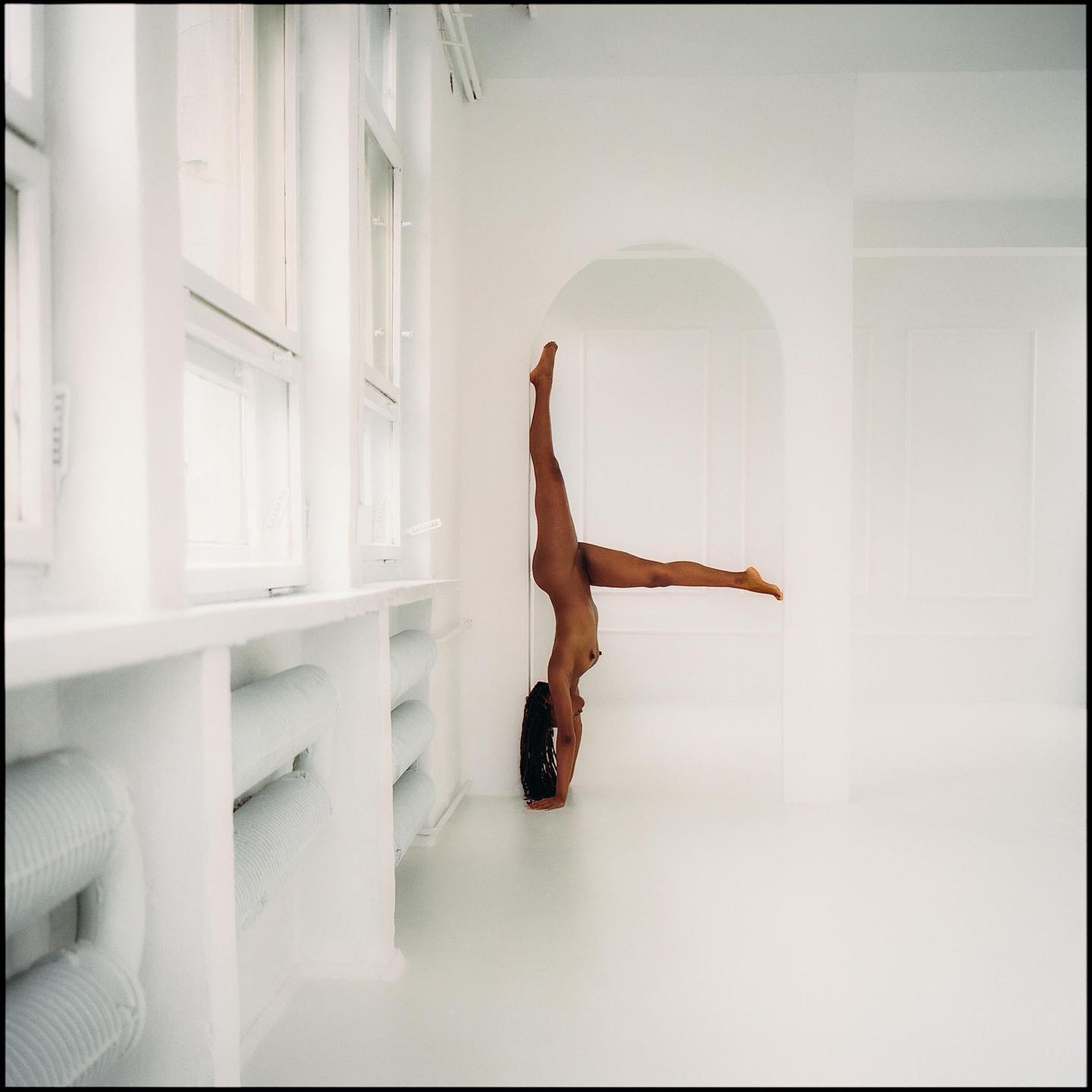 A woman performs a handstand in a minimalist white room.