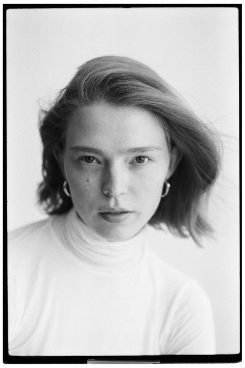A woman with short hair and a turtleneck looks directly at the viewer.