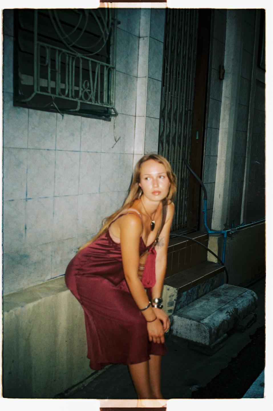 A woman in a red dress sits on a ledge next to a building at night.