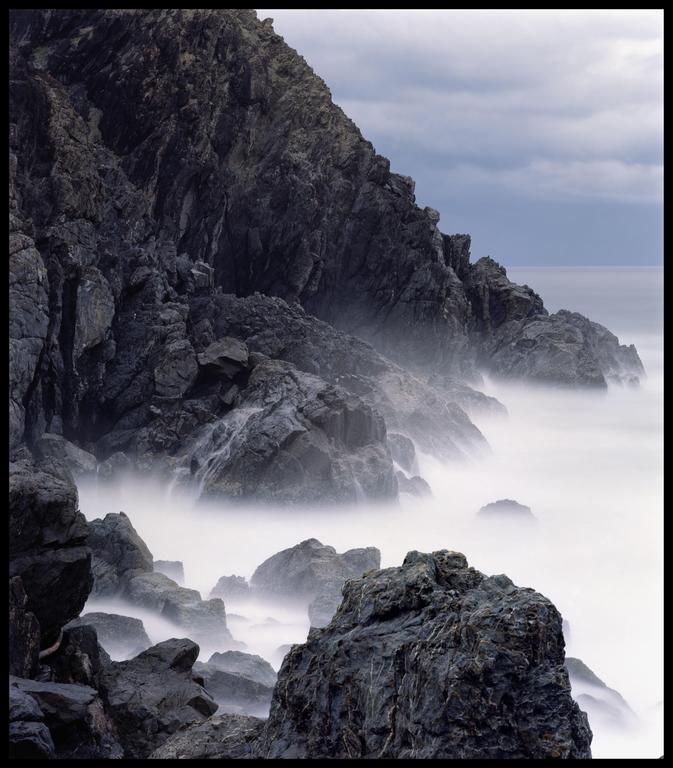 Waves crash against a rocky cliff, creating a misty effect over the water.