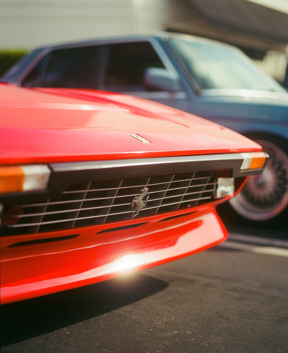 The front of a red car with a silver emblem on the grille is parked in front of another car.
