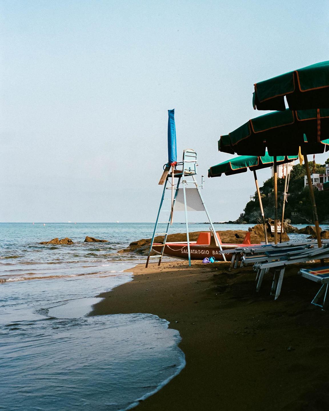 A lifeguard stand and several beach umbrellas stand on a sandy beach next to the ocean.