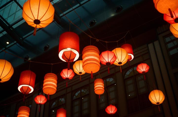 Many red and orange lanterns hang from a ceiling with a building visible in the background.