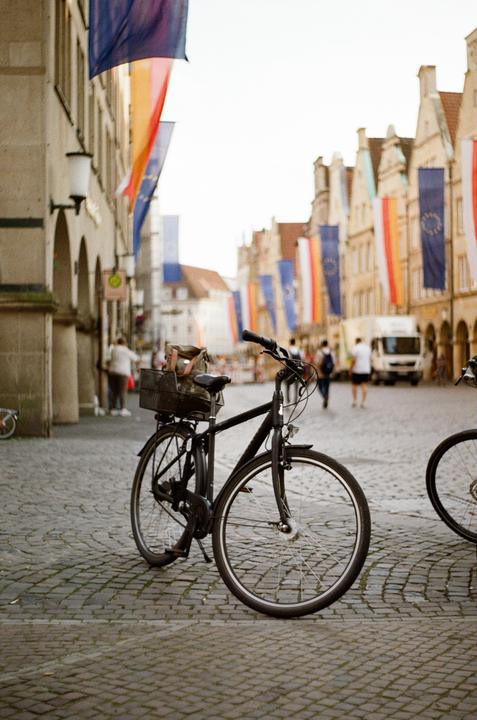 A bicycle is parked on a cobblestone street lined with buildings adorned with flags.