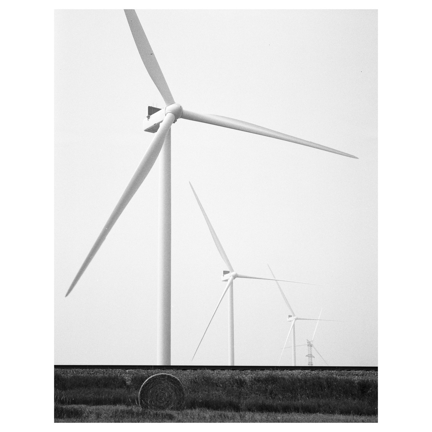 Three wind turbines stand in a field with a hay bale in the foreground.