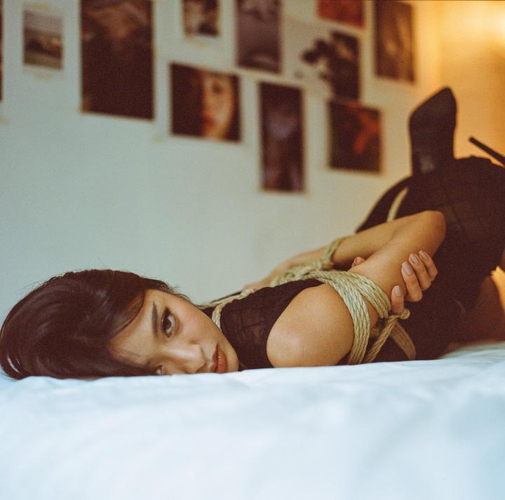 A woman with her arms tied with rope lies on a bed.