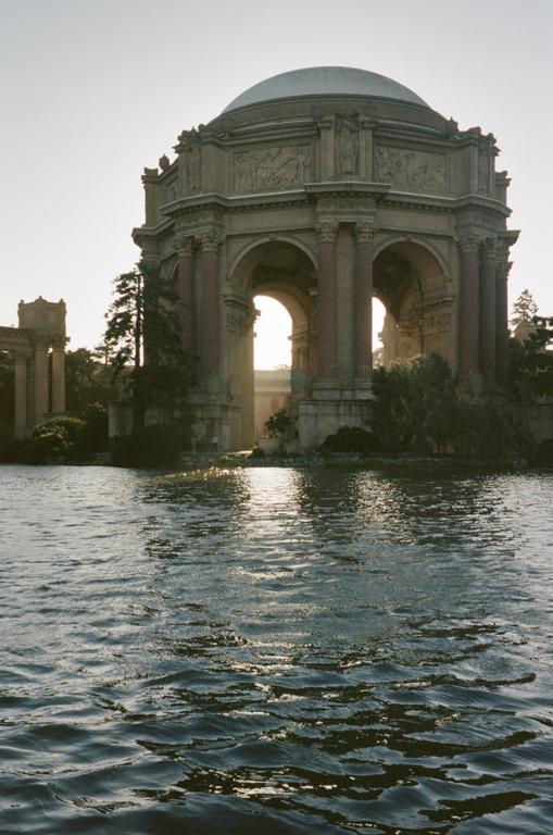 A large domed building with arches stands next to a body of water, with sunlight shining through one of the arches.