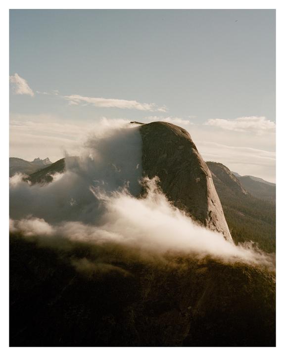 Clouds partially obscure a large rock formation in a mountainous landscape.