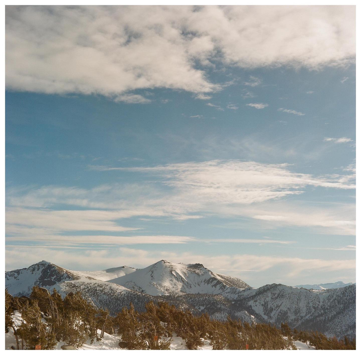 Snow-covered mountains and trees are visible under a blue sky with clouds.
