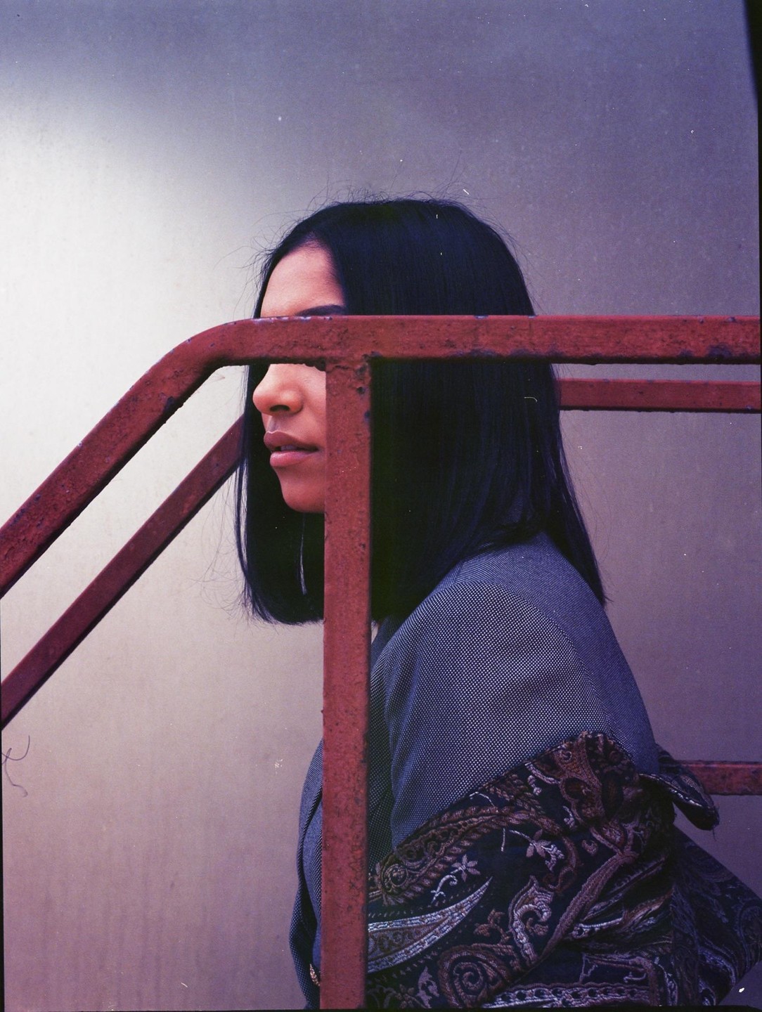 A woman with dark hair is partially obscured by a rusty red railing.