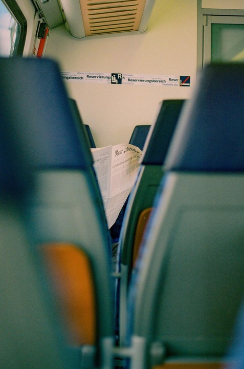 A newspaper is visible between two rows of seats on a train.