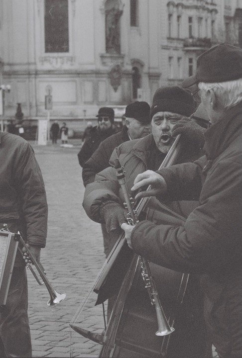 A group of men play musical instruments on a cobblestone street in front of a building.