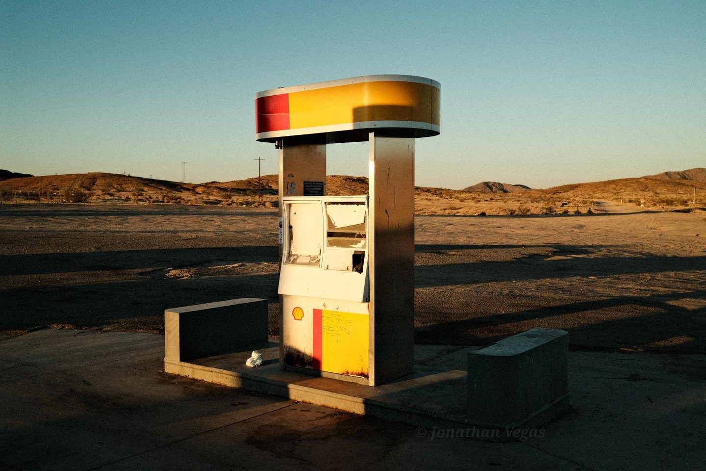 An abandoned gas pump stands in a desert landscape under a clear sky.