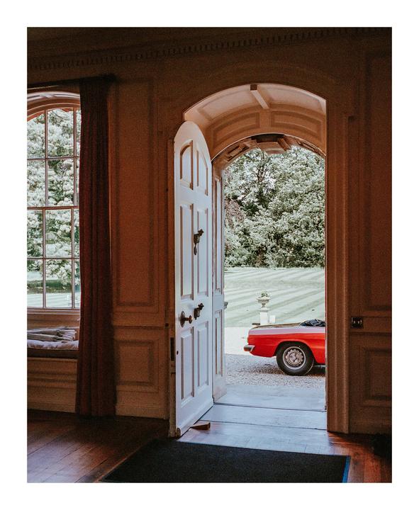 A red car is parked outside a building with an open door and a large window.