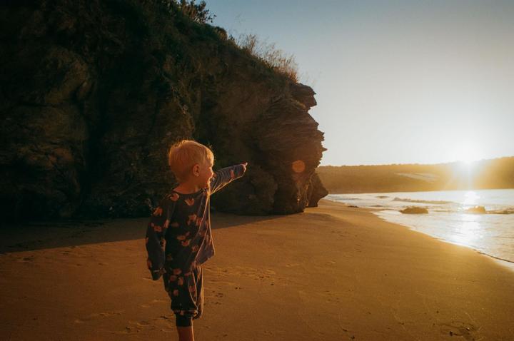 A child points towards the ocean on a beach at sunset.