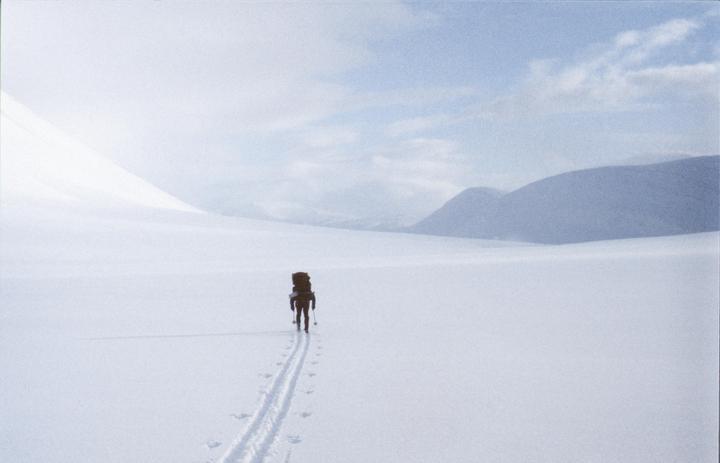 A person with a large backpack skis across a vast, snow-covered landscape with mountains in the distance.
