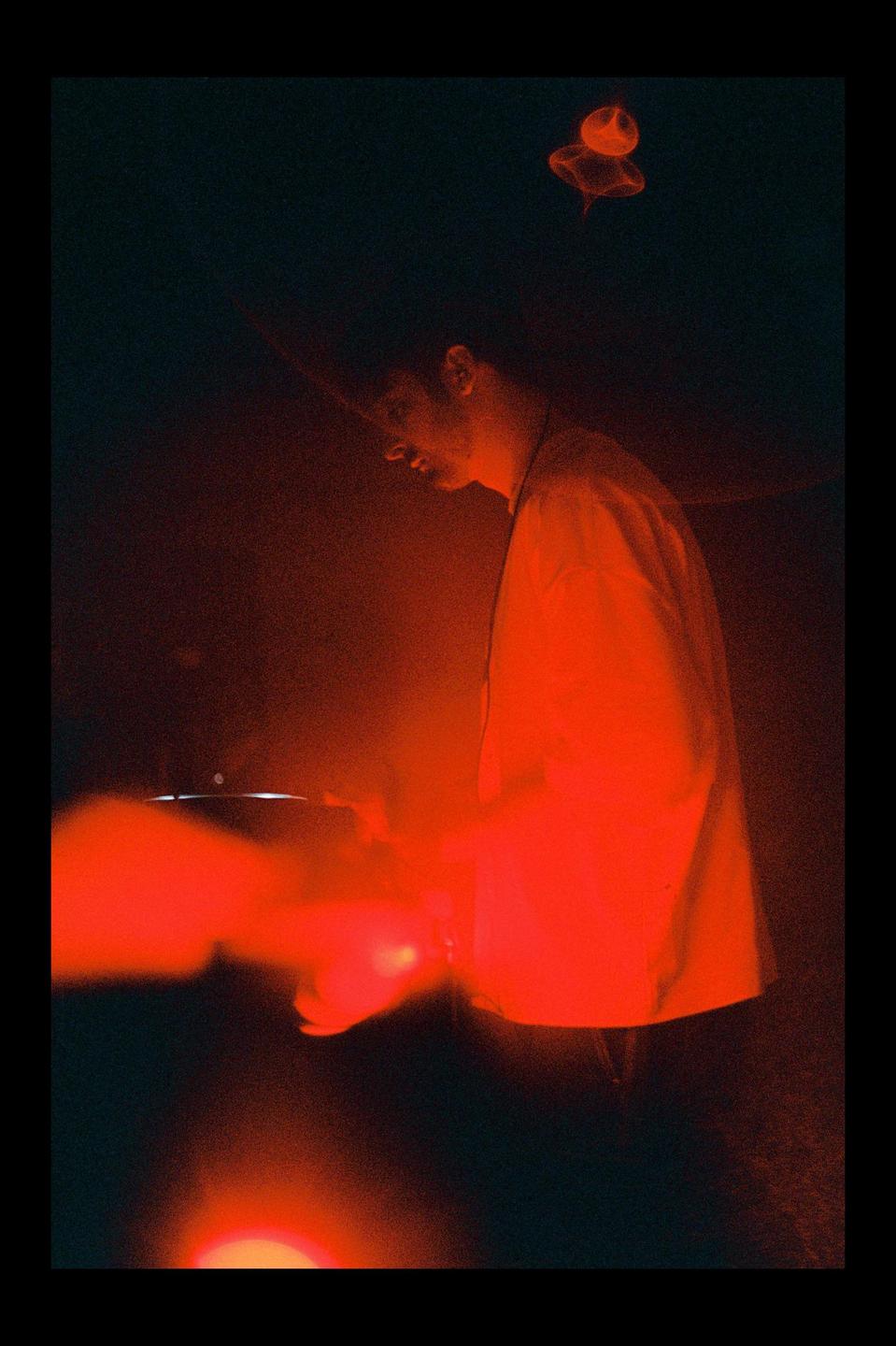 A man is illuminated by red light while DJing in a dark room.