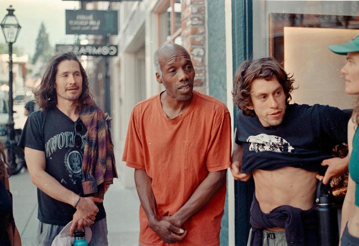 Three men and a woman are standing on a street next to a building with a sign that says "COWBOY" in reverse.